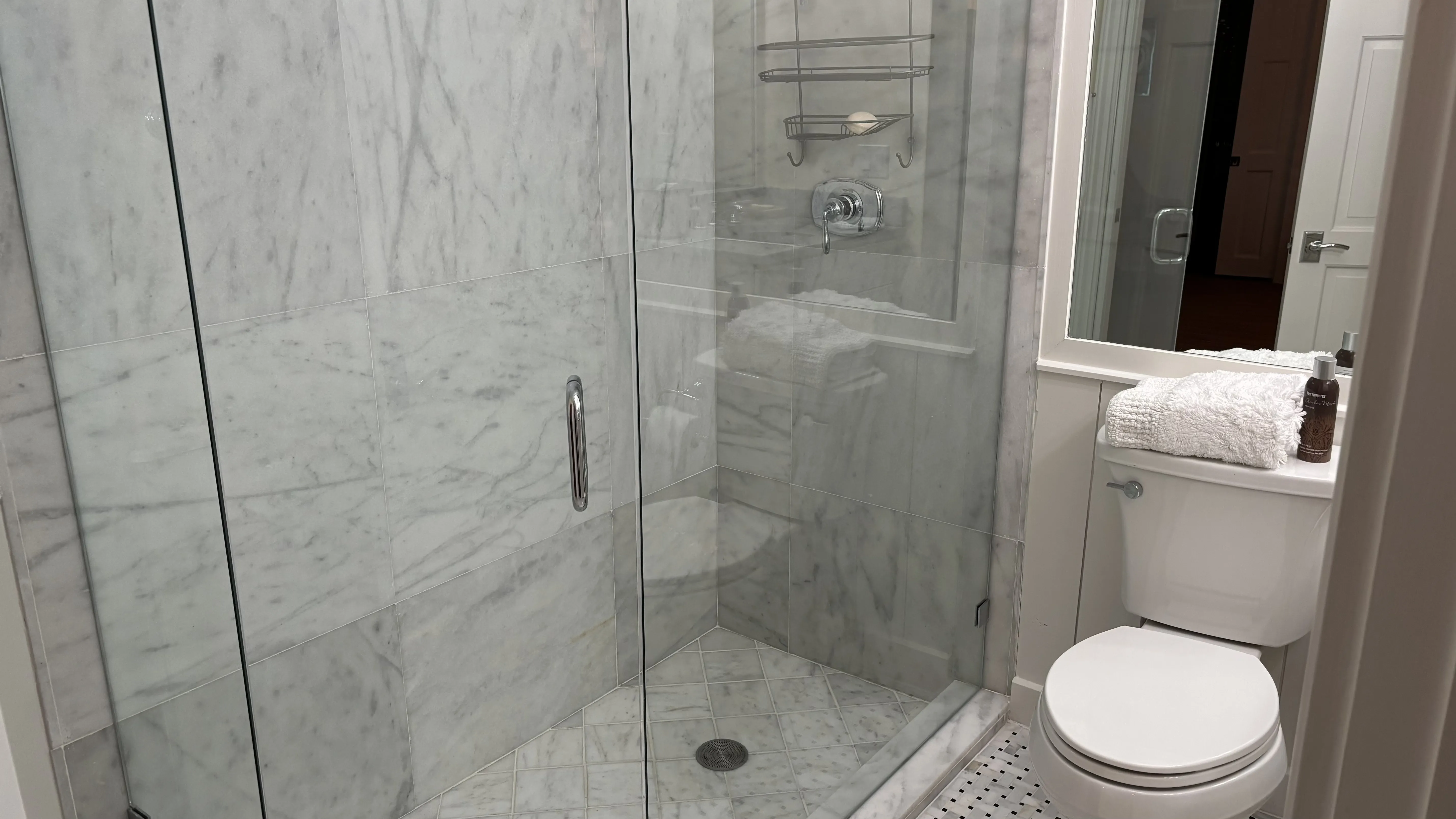 Modern bathroom featuring a glass shower, marble walls, and a white toilet.