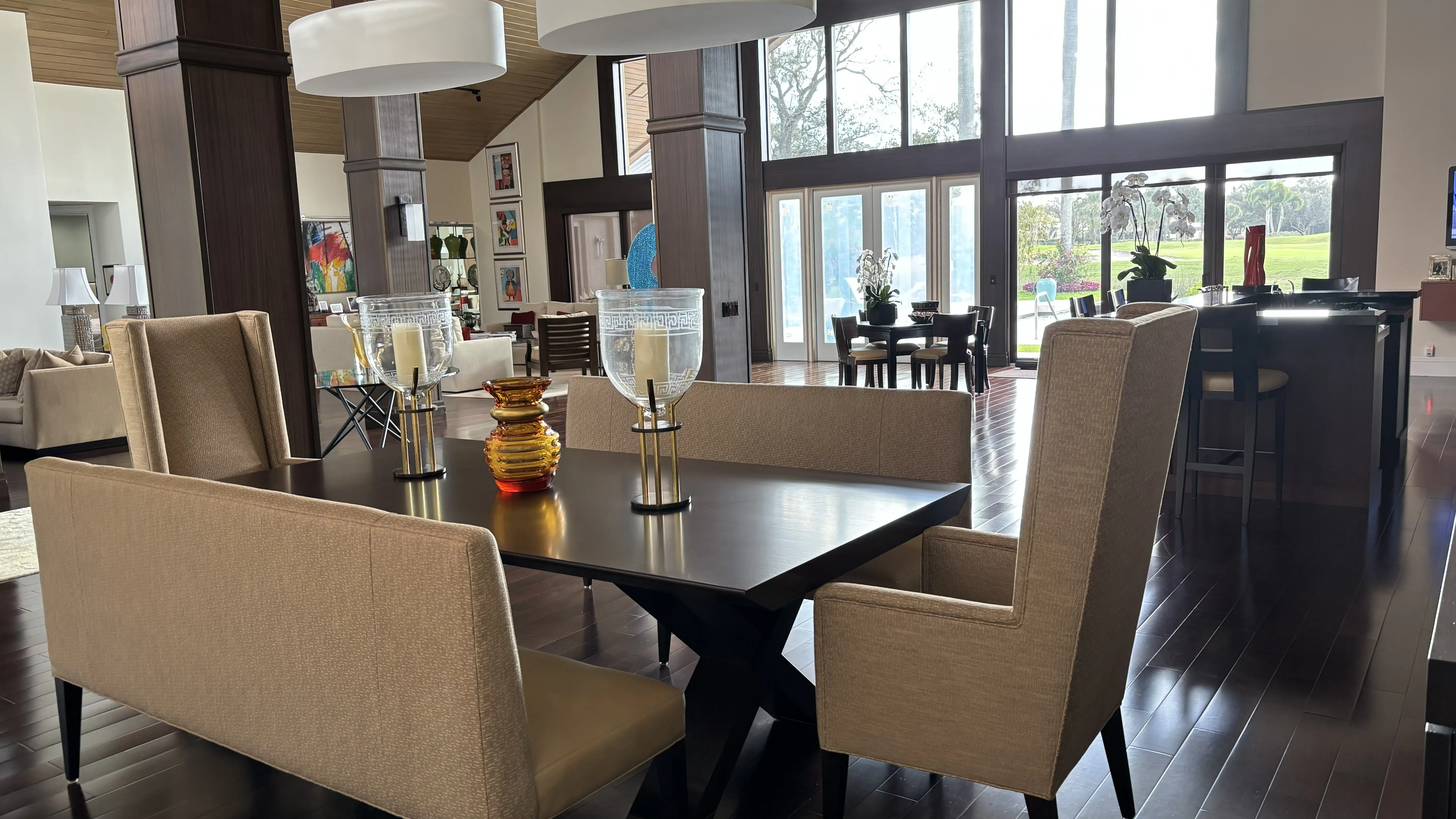 Modern dining room with a large table, beige chairs, and a view of greenery.